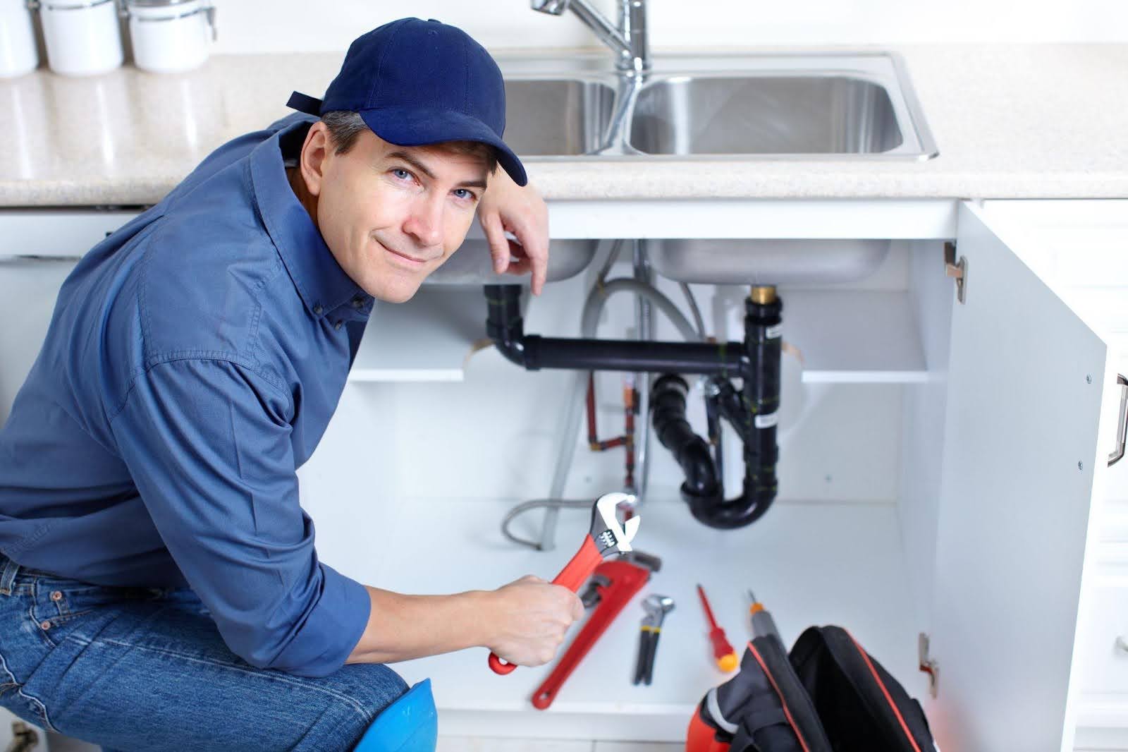 A man wearing a blue shirt and hat is repairing a sink, demonstrating his skills in plumbing maintenance