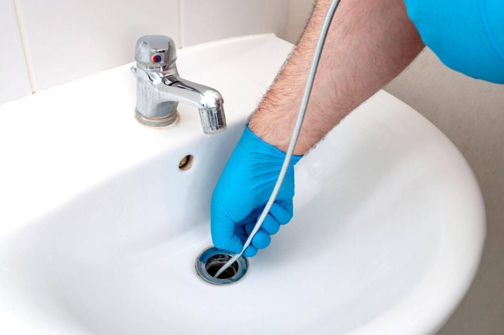 A person wearing blue gloves cleans a sink using a hose ensuring it is free of dirt and debris