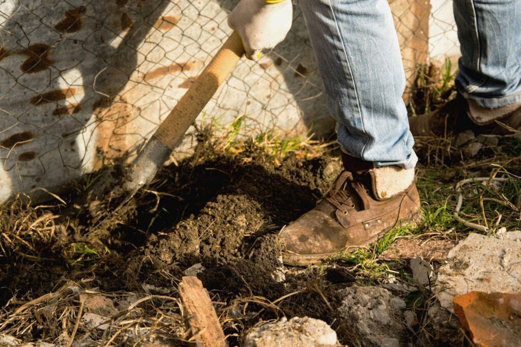 A person using a shovel to dig a hole in the ground focused on their task in an outdoor setting