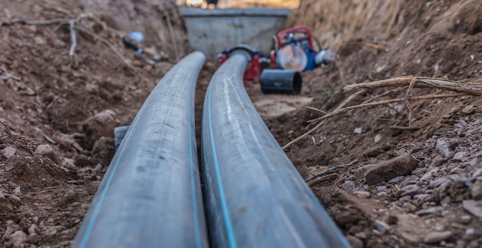 Pipes are positioned in the dirt beside an open trench indicating ongoing construction or utility work