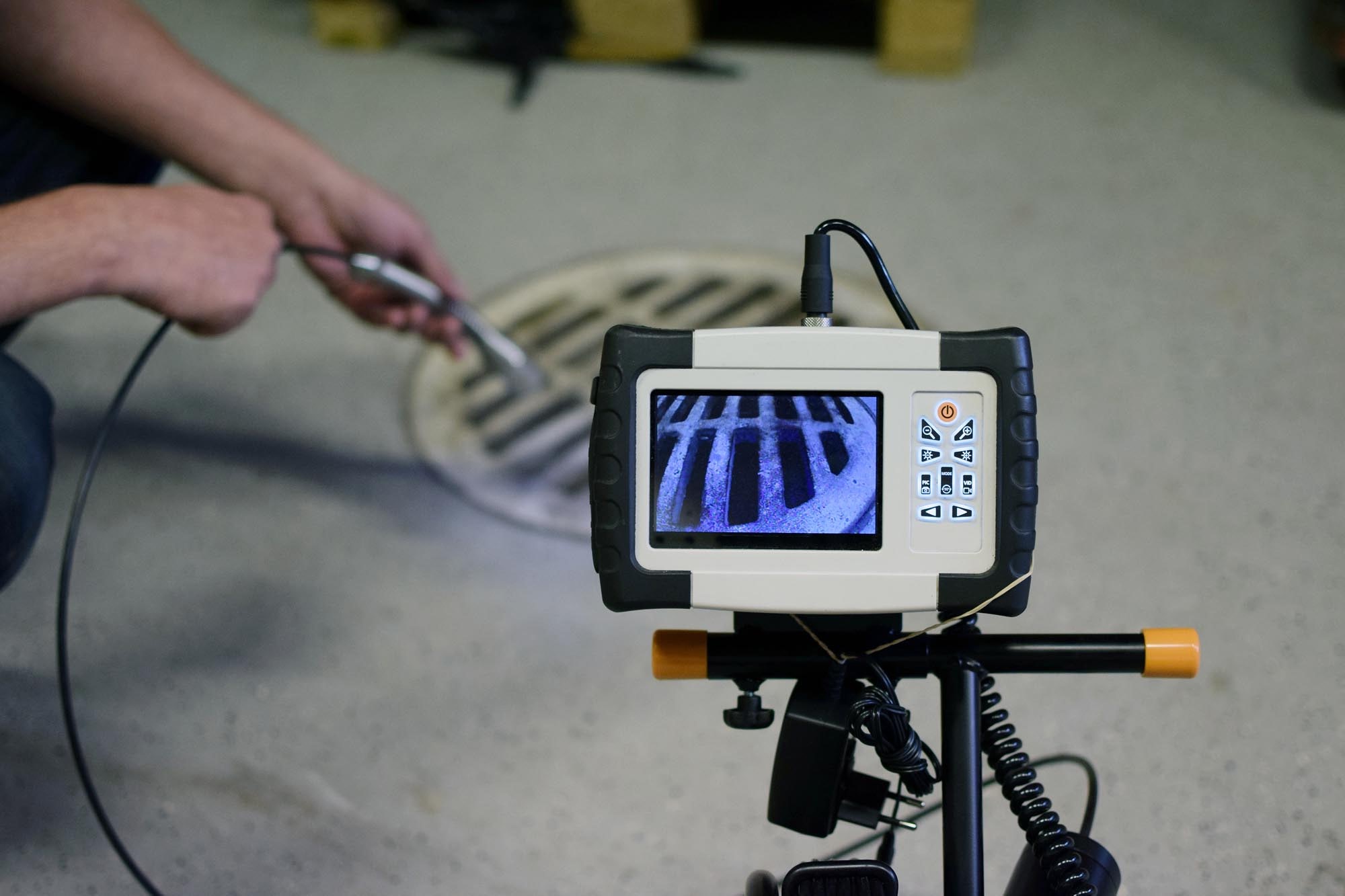 A technician uses a video inspection camera to examine a drain, showcasing the camera's display and the drain's interior.
