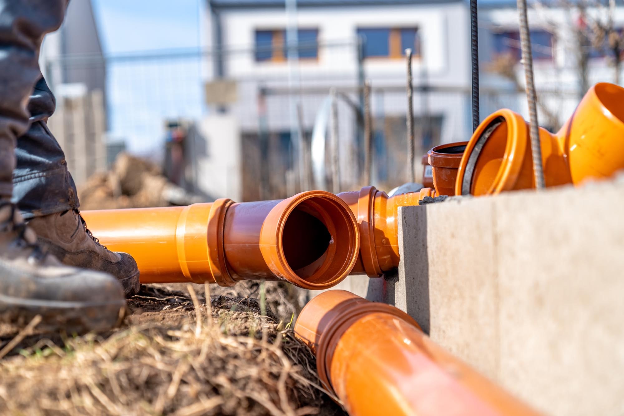 Construction site featuring orange drainage pipes being installed, showcasing plumbing work and groundwork preparations.