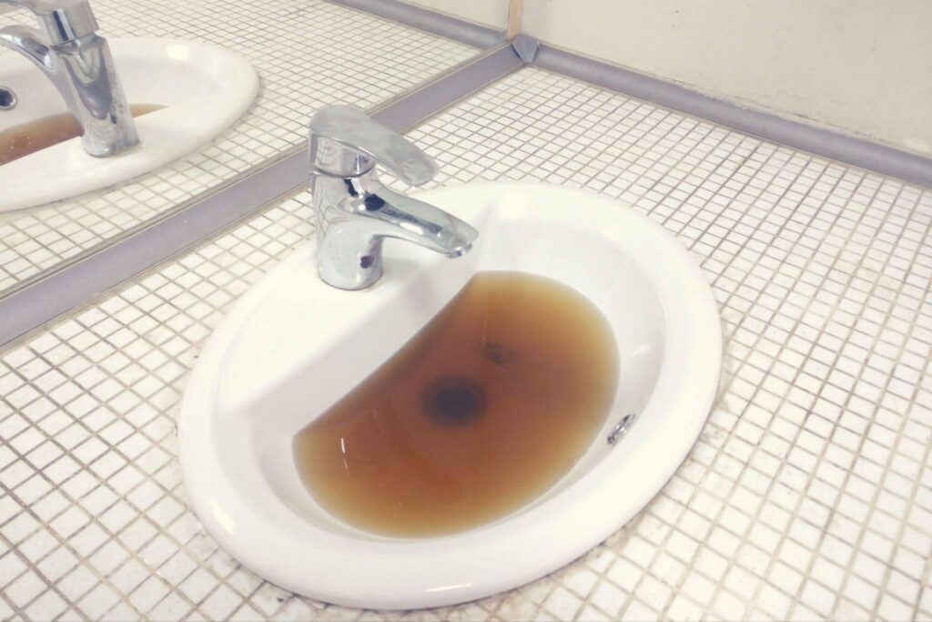 A bathroom sink with brown, murky water indicating potential plumbing issues or contamination.