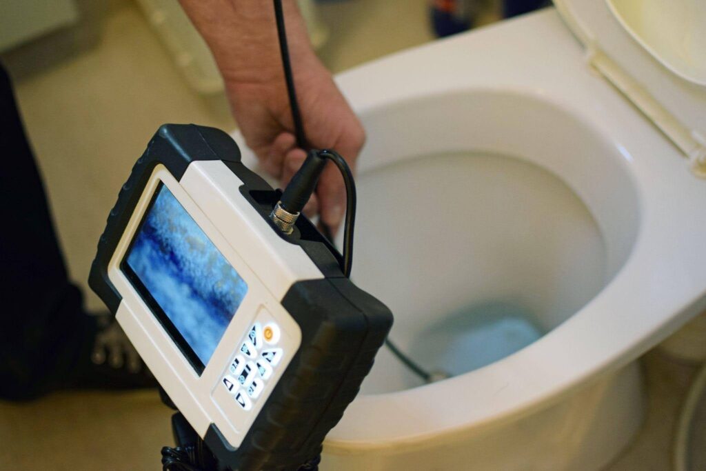A plumber uses a video inspection camera to check a toilet for clogs and plumbing issues, ensuring proper maintenance.