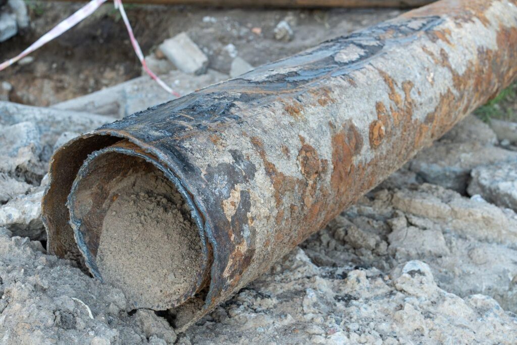 A pipe lying on the ground marked with red and white caution tape for safety and visibility