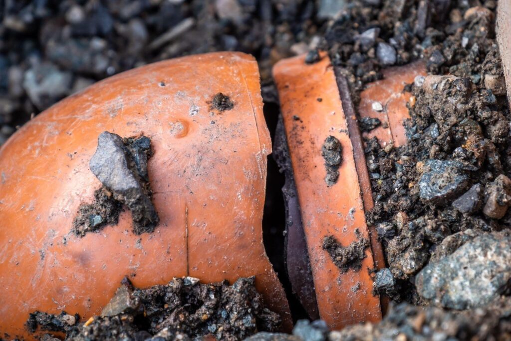 A damaged blue underground water pipe is exposed in a soil trench with a large jagged crack