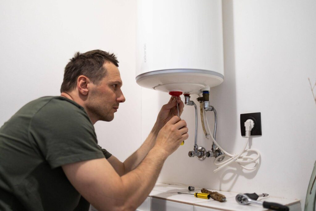 A-man-repairs-a-water-heater-in-a-bathroom-surrounded-by-tools-and-plumbing-equipment.