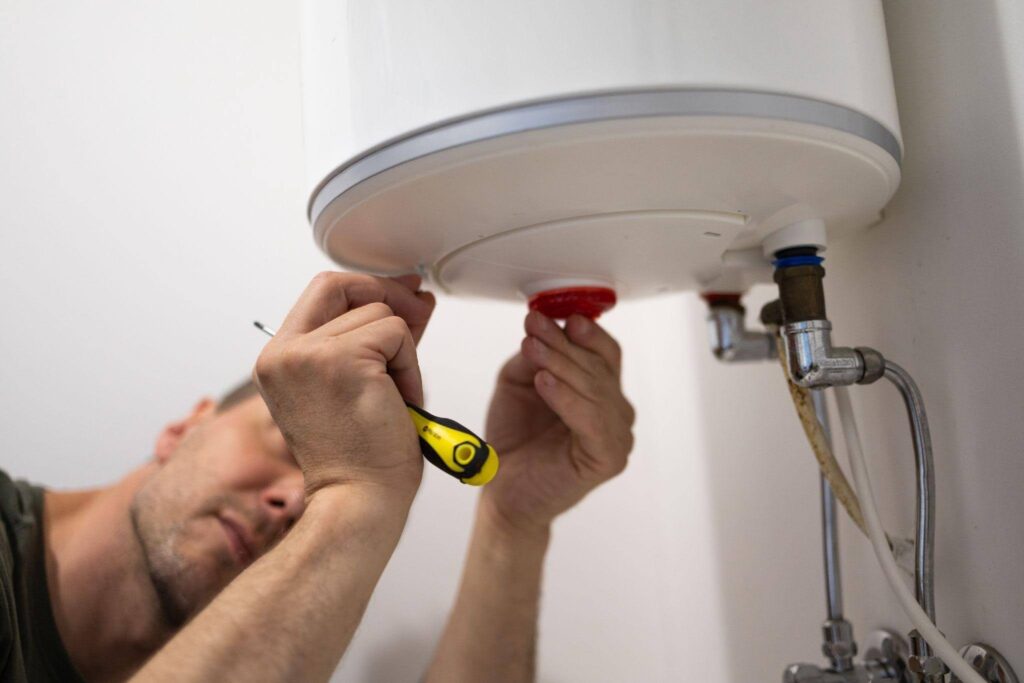 A technician works on a water heater adjusting components with tools in a residential setting